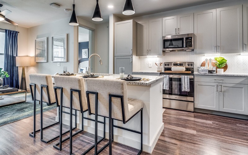One-Bedroom Apartments in Grand Prairie, TX - Aven at the Cove - Modern Kitchen with Wood-Style Flooring, Stainless Steel Appliances, Granite Countertops, White Tile Backsplash, Grey Cabinets, and a Kitchen Island